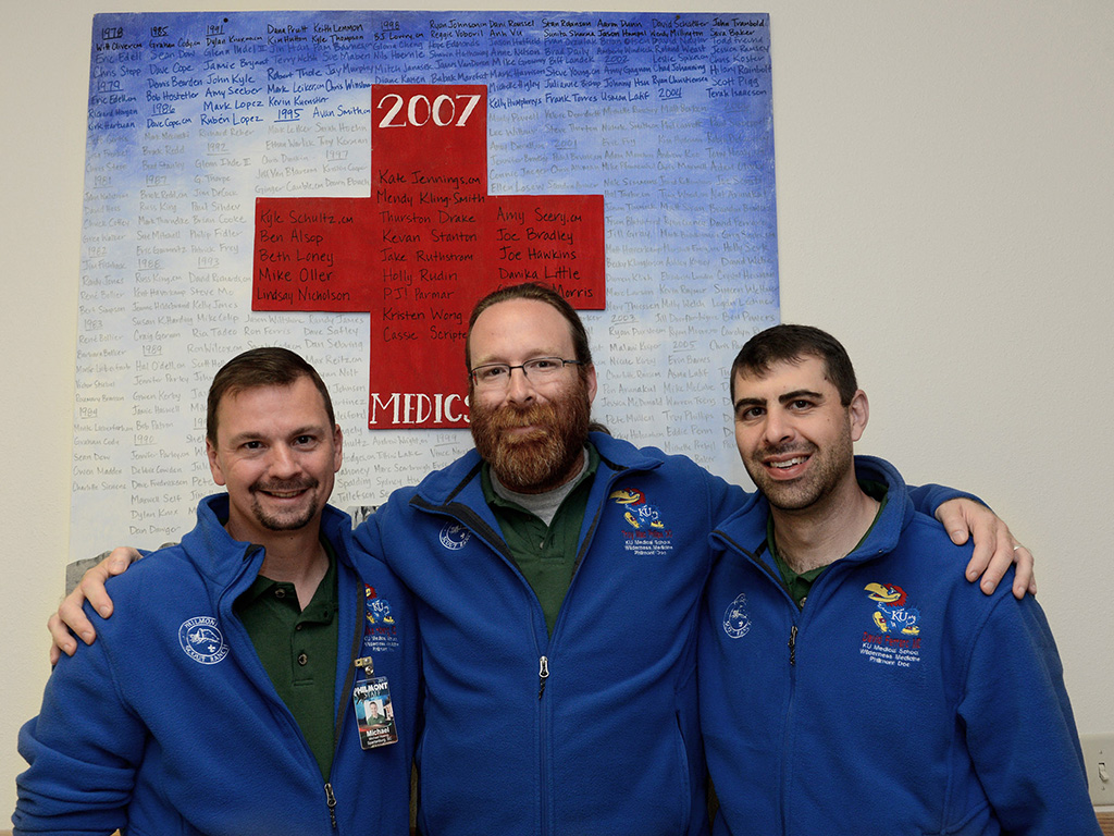 Three men posing together in front of a red medical cross